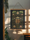 26x36 inch vertical wall tapestry printed on silky polyester fabric, featuring a detailed embroidered-style beetle surrounded by pink and green florals and curling botanical vines on a black background, with wooden hanger and twine at top and bottom. Art nouveau, vintage-inspired, cottagecore, gothic decor.